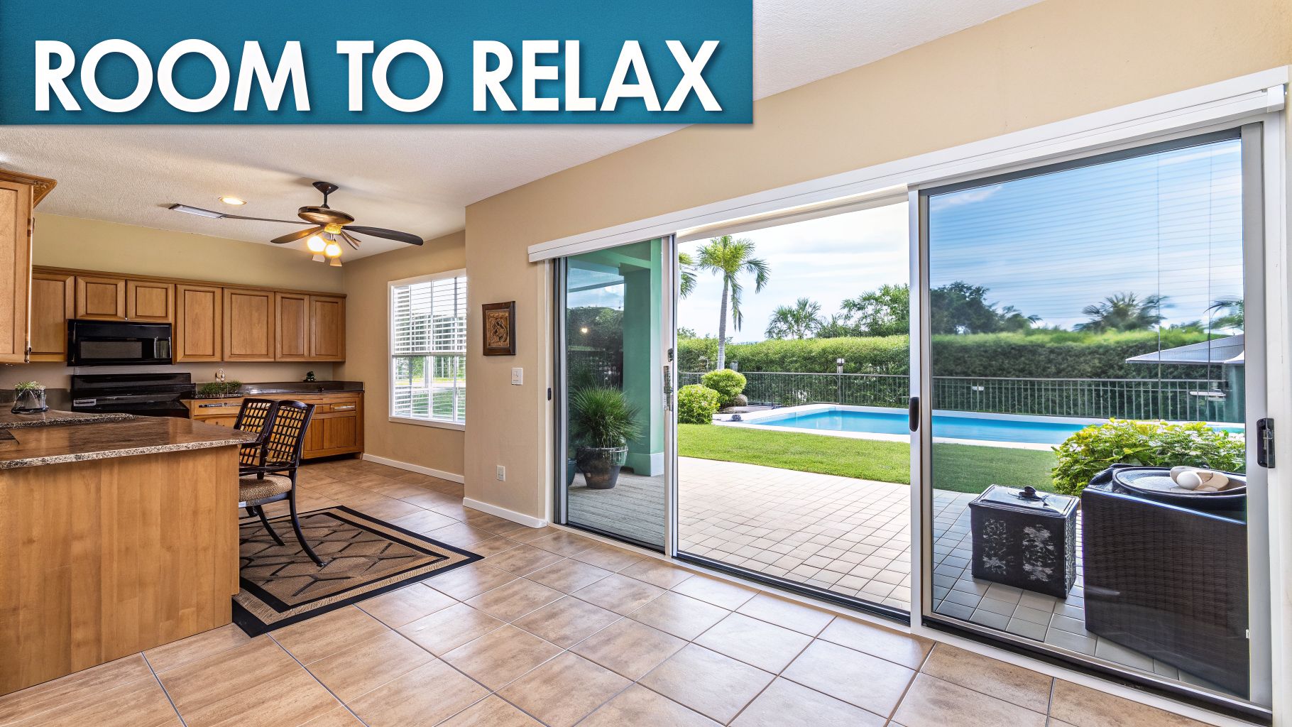 A bright kitchen with a breakfast bar opens to a patio, pool, and palm trees, offering space to relax.