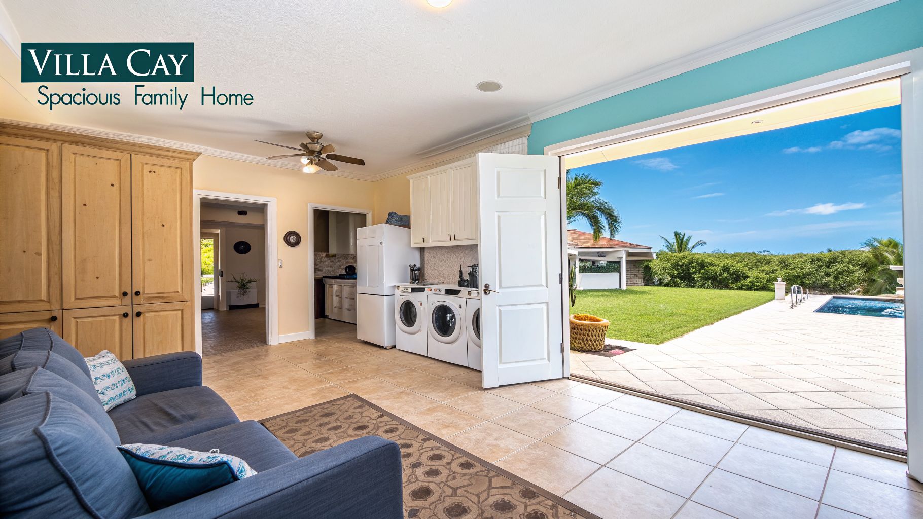 Spacious family home interior with a laundry area, blue sofa, and open doors to a pool and garden.