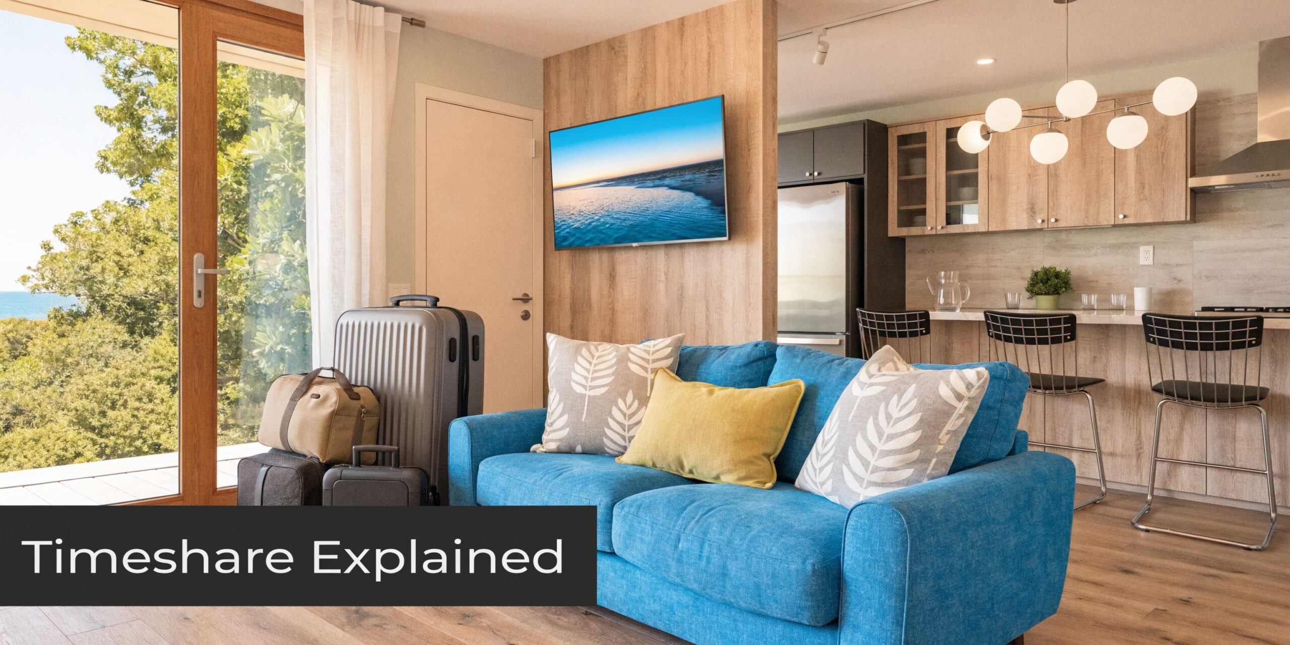 A modern vacation rental living room featuring a blue sofa, luggage, and a kitchen area.